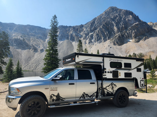 Silver Ram truck with a Palomino truck camper setup by a stunning mountain lake, ideal for an RV rental adventure.