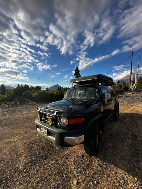 A black Toyota FJ Cruiser with a rooftop tent on a dirt road. Perfect for your next adventure or a unique RV rental experience.
