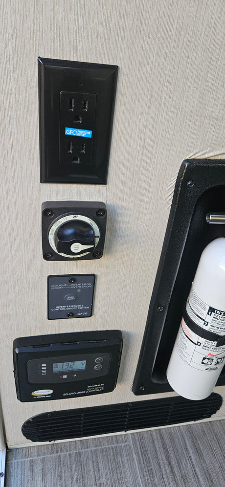 RV rental control panel: GFCI outlet, battery switch, inverter remote, solar charger, and fire extinguisher.