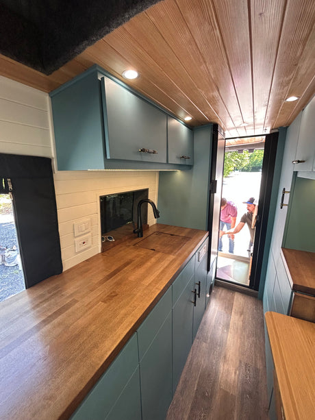 RV rental's modern kitchen: wood counters, teal cabinets, and ample storage in a custom conversion.