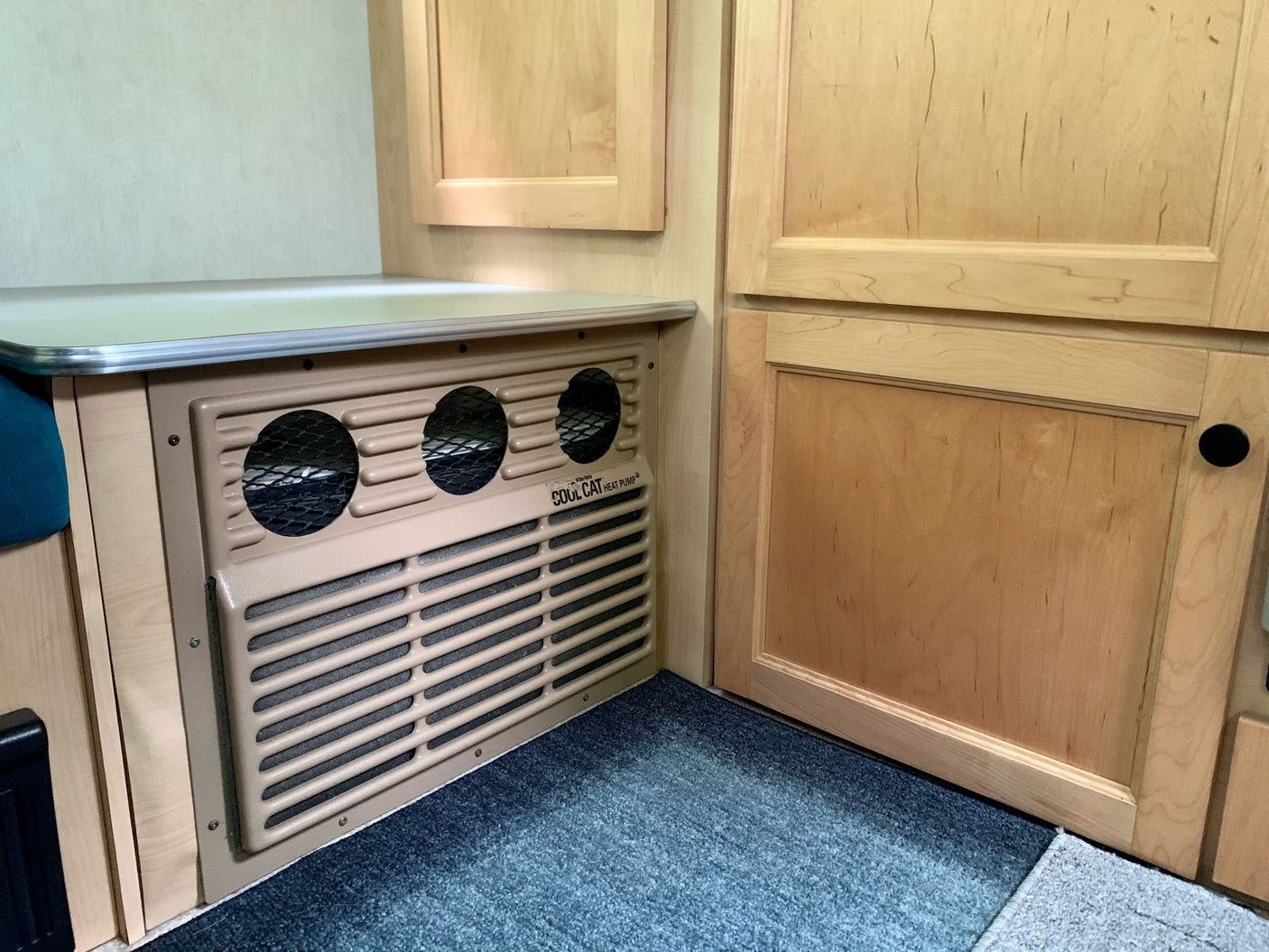 Compact RV rental interior featuring a built-in Cool Cat heat pump unit, wood cabinetry, and a countertop.