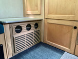 Compact RV rental interior featuring a built-in Cool Cat heat pump unit, wood cabinetry, and a countertop.