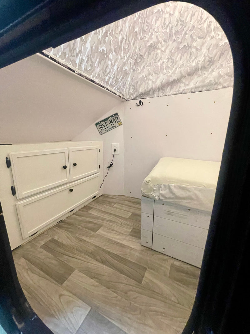 Inside a compact RV rental: white cabinets, bed with storage base, wood-look floor, and a camo ceiling. — photo 9