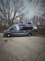 Gray Mercedes Sprinter RV with tree reflections on windows, parked in nature. Ideal rv rental for adventure.