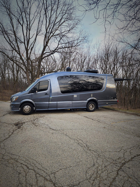 Gray Mercedes Sprinter RV with tree reflections on windows, parked in nature. Ideal rv rental for adventure.
