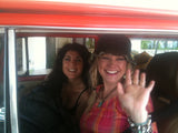 Two smiling women inside an RV rental. The blonde woman in a hat waves, while her dark-haired friend smiles nearby.