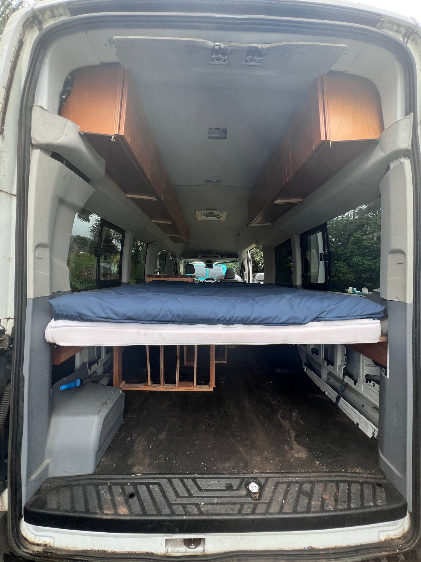 Spacious RV rental van conversion: elevated bed, under-bed storage, and overhead wooden cabinets for comfortable travel.