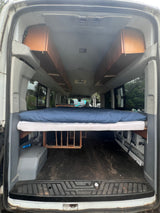 Spacious RV rental van conversion: elevated bed, under-bed storage, and overhead wooden cabinets for comfortable travel.