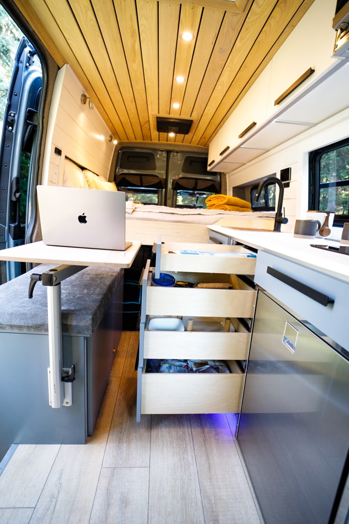  and a dining table.|Enjoy an RV rental adventure! A person relaxes on a cozy bed inside a van — photo 18