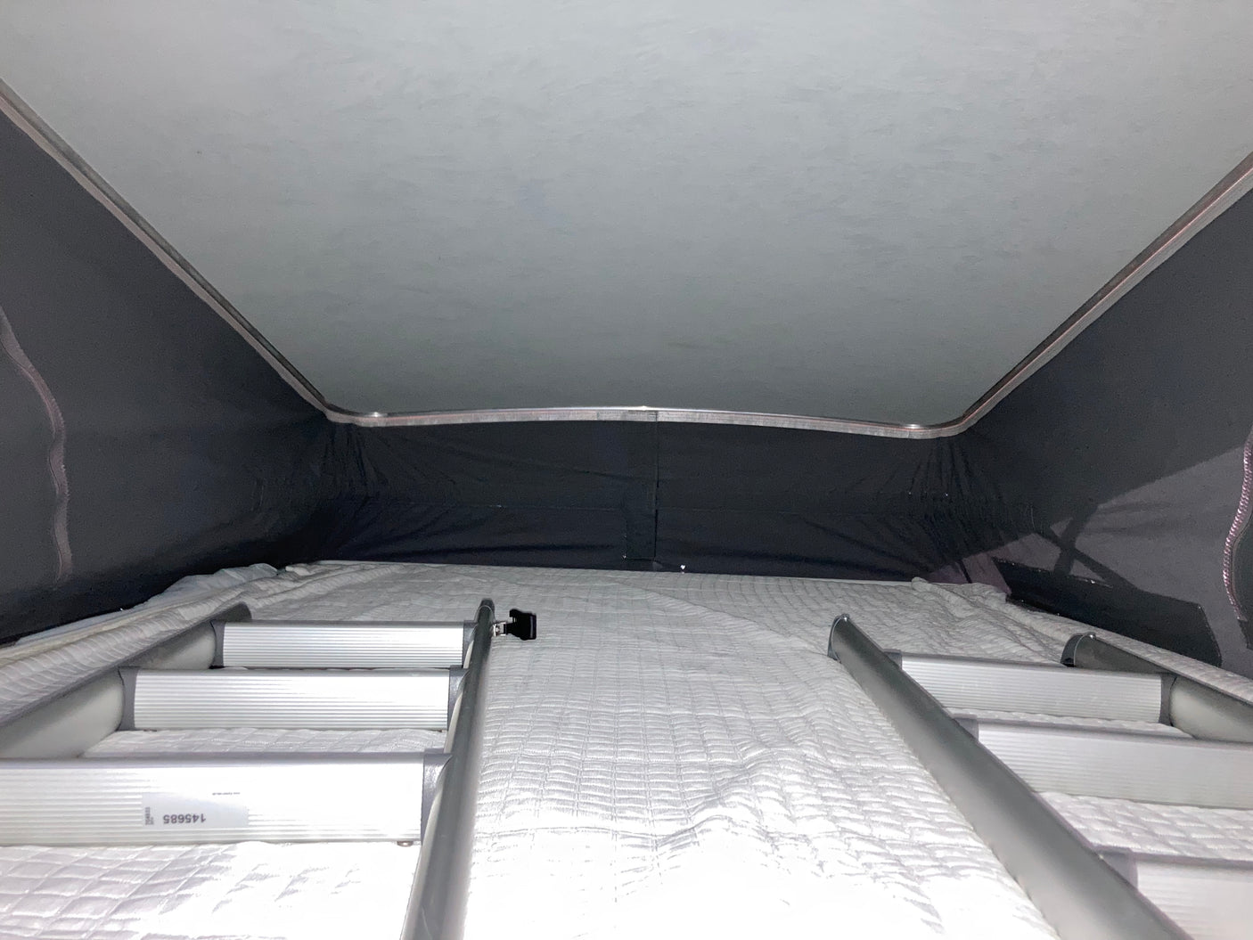 Inside an RV rental pop-top camper, showing the upper bed with a white mattress and access ladders.