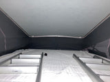 Inside an RV rental pop-top camper, showing the upper bed with a white mattress and access ladders.