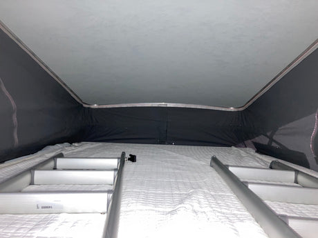 Inside an RV rental pop-top camper, showing the upper bed with a white mattress and access ladders.