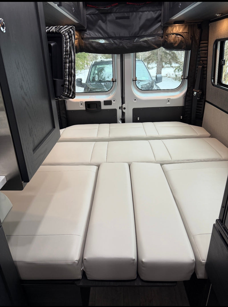 Comfortable white modular bed cushions fill the rear of this RV rental, with winter scenery visible through the back windows. — photo 7