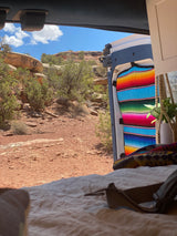 RV rental view: looking out a camper van door at a red rock desert with sparse trees under a blue sky.