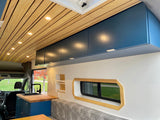 Experience this bright RV rental's modern interior: custom wood slat ceiling, blue cabinets, kitchen with sink, and unique window.