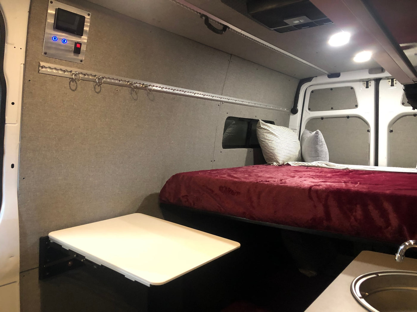 Inside this RV rental: a cozy bed, control panel, fold-down table, and small sink for compact living. — photo 10