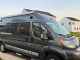 Gray camper van rv rental, ready for travel. Shows roof awning, side steps, and tinted windows in a residential setting.