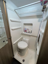 Compact RV rental wet bath featuring a toilet, handheld shower, and handy storage alcove with toilet paper.