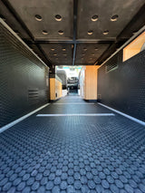 Spacious RV rental van interior with durable, textured flooring & sidewalls. Modular design, wood accents, and perforated ceiling visible.