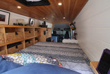 Inside a stylish RV rental, showing the bed, wood ceiling, white walls, and built-in storage with wicker baskets.