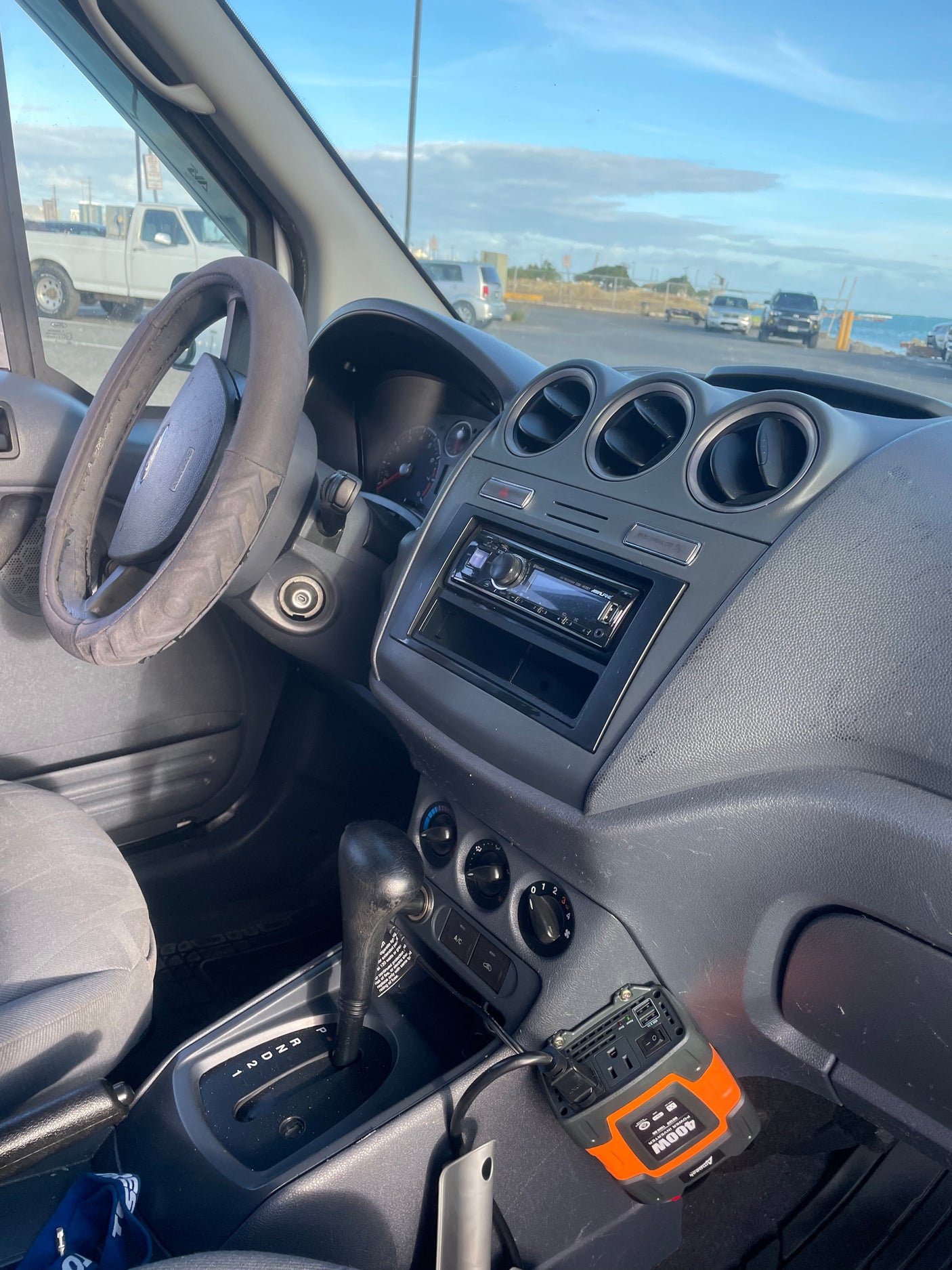 Interior of an **rv rental** van showing a worn steering wheel, dashboard, and a 400W power inverter. Ocean view outside.