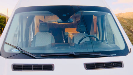 Front view of a white rv rental camper van, with a noticeable crack in the windshield. Inside, seats and a custom interior are visible.