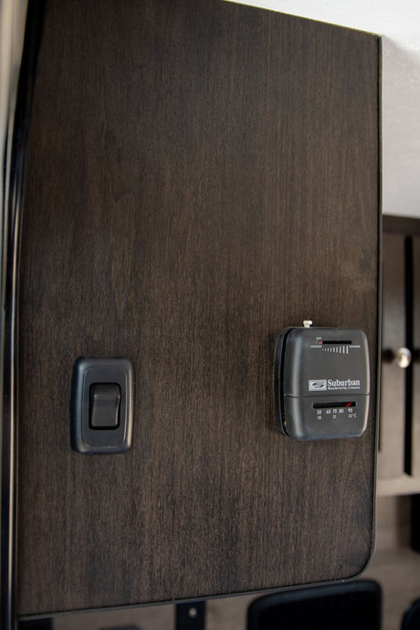 RV rental interior: A Suburban thermostat and light switch on a dark wood panel, showing temperature controls.