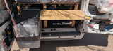 Rear view inside an RV rental van showing a Dometic cooler, wooden kitchen area with water tanks, and organized storage.