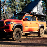 An orange Toyota Tacoma overlander, equipped with a rooftop tent & awning. A ready RV rental for your next outdoor adventure.