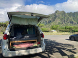 Cozy campervan with bed setup in converted minivan, parked against lush green mountains. Ideal for an RV rental or scenic travel adventure.