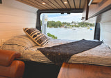 Cozy RV rental interior with a bed and a stunning view of a tranquil harbor, dotted with boats. Perfect for a scenic escape.