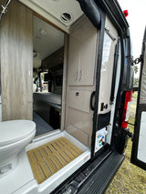 Inside this modern RV rental: open rear view reveals compact kitchen/storage, control panel, and bathroom beyond.