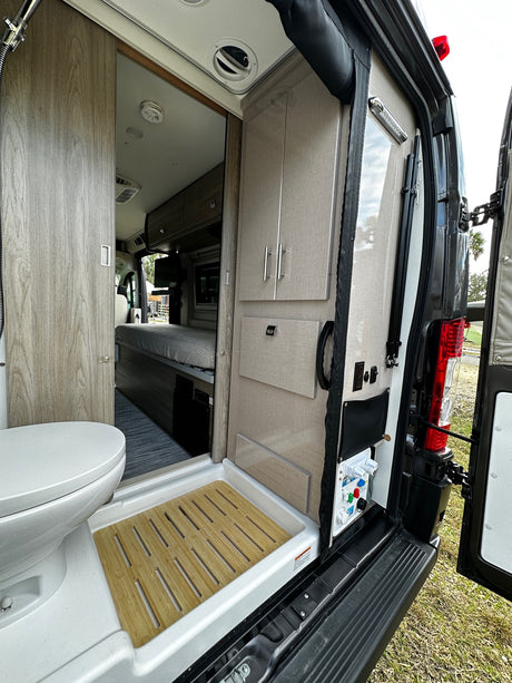 Inside this modern RV rental: open rear view reveals compact kitchen/storage, control panel, and bathroom beyond.