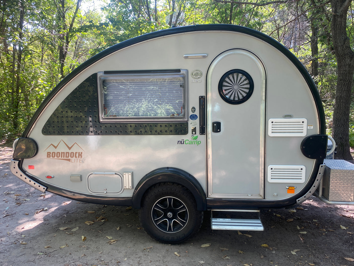 Grey nuCamp T@B 320 Boondock Lite teardrop camper for rv rental, parked in a wooded area. Great for outdoor adventures.