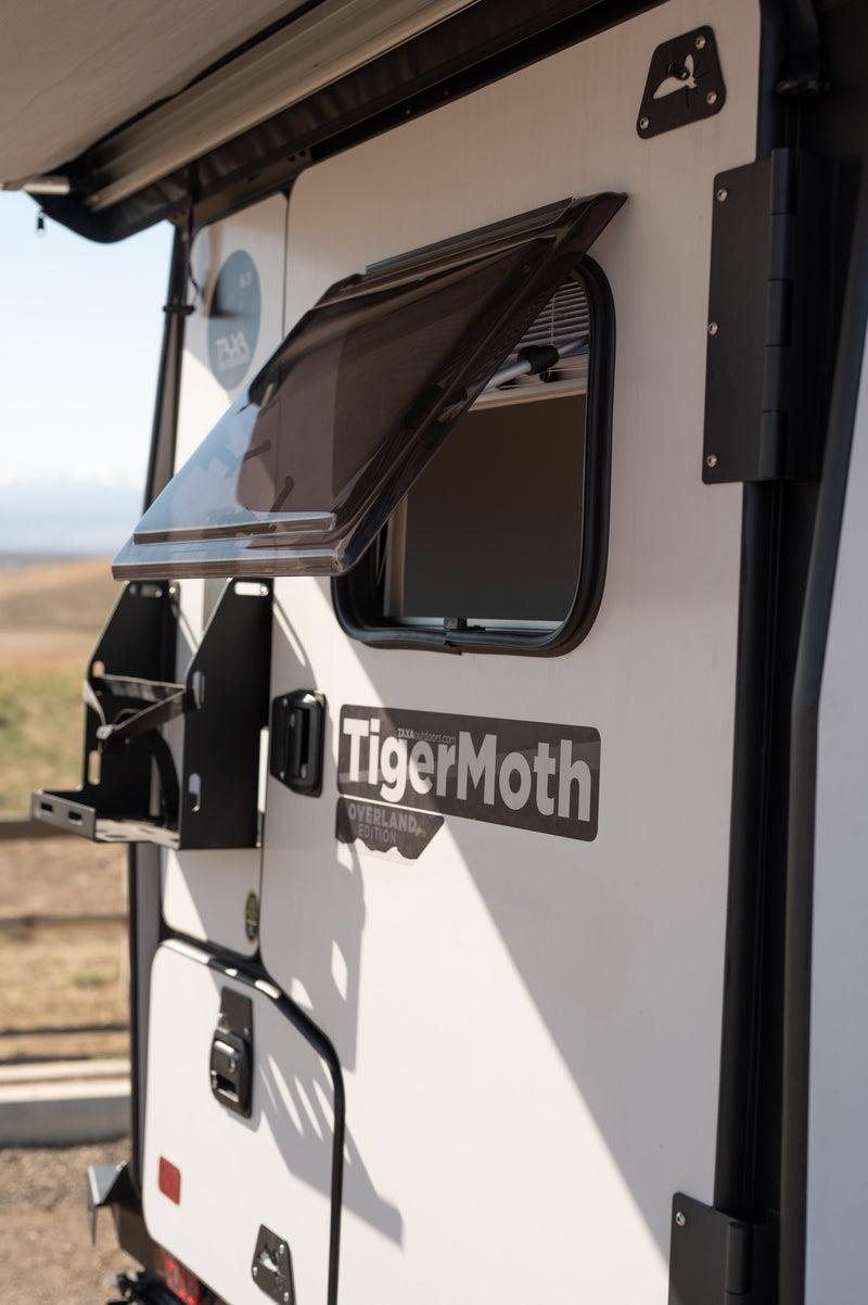 ideal for outdoor trips.|Close-up of a white and black TigerMoth overland trailer with off-road tires and roof racks. Ideal for an RV rental outdoor adventure.|A white and black TigerMoth overland trailer — photo 4