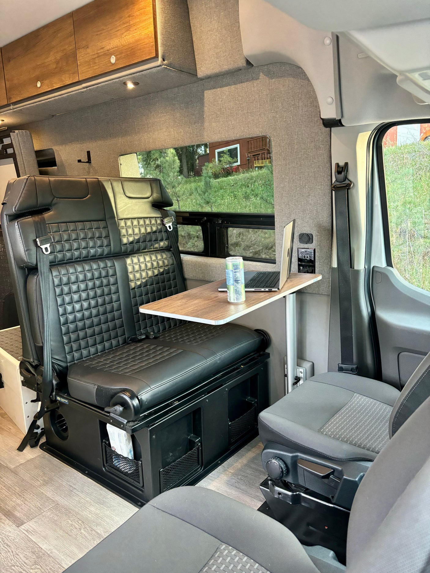 Inside a modern rv rental: quilted leather seats, laptop on table by large window. Ideal for remote work/travel comfort.