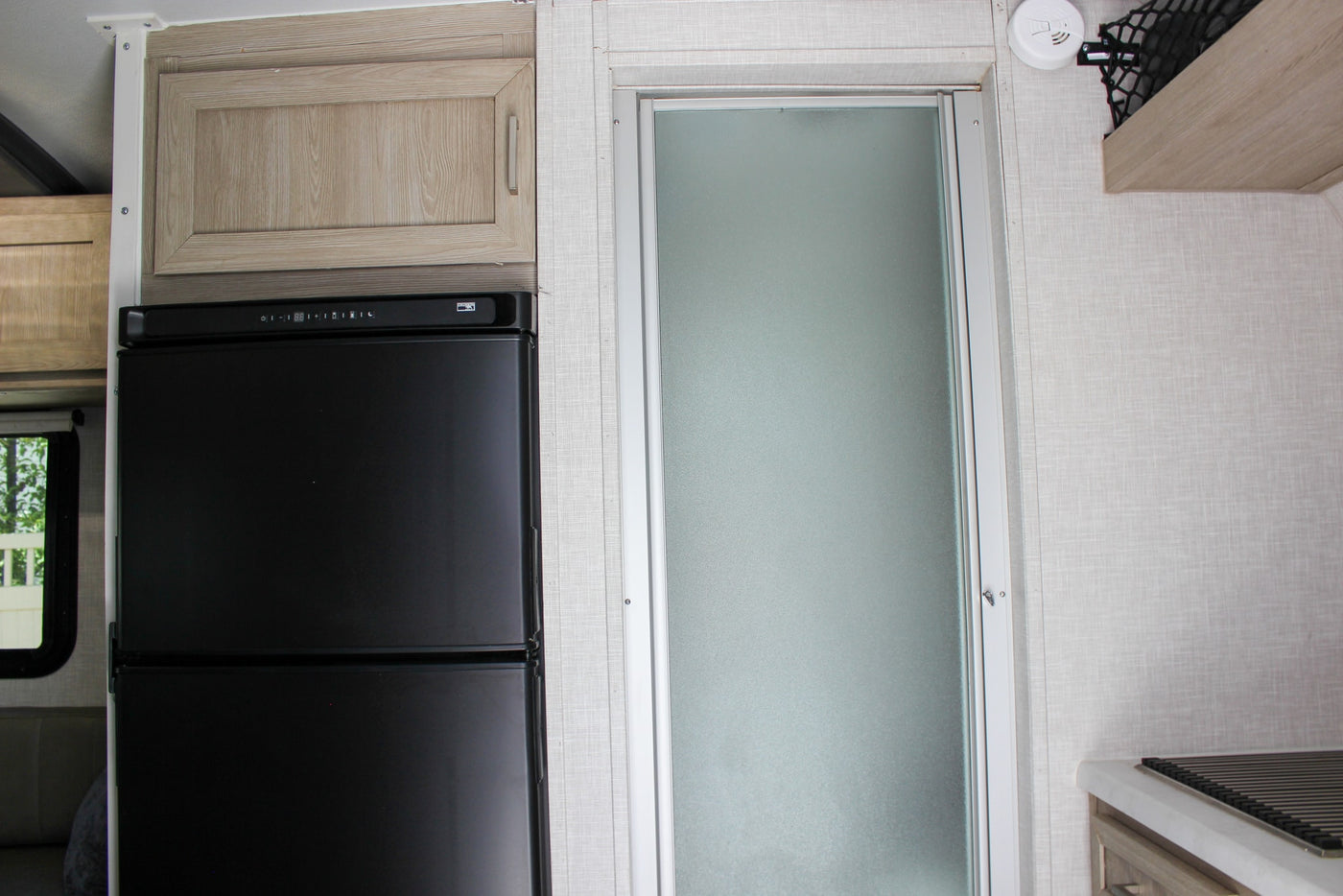 This rv rental interior features a black refrigerator, light wood cabinets, and a frosted glass shower door, ideal for mobile living. — photo 17