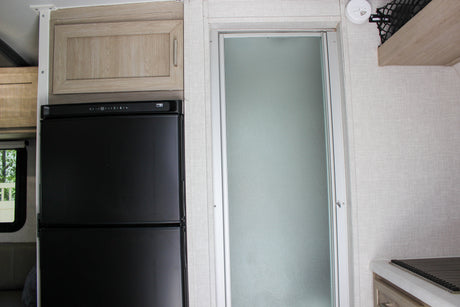 This rv rental interior features a black refrigerator, light wood cabinets, and a frosted glass shower door, ideal for mobile living.