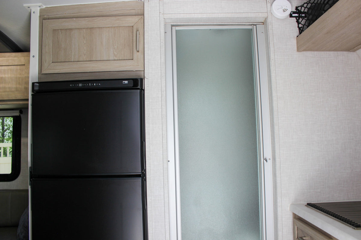  and a glass vase with green plant stems.|An RV rental kitchen features a compact stove with a frying pan — photo 37
