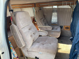 Interior of an RV rental showing two plush captain's chairs, wood trim, and privacy curtains for comfortable travel.