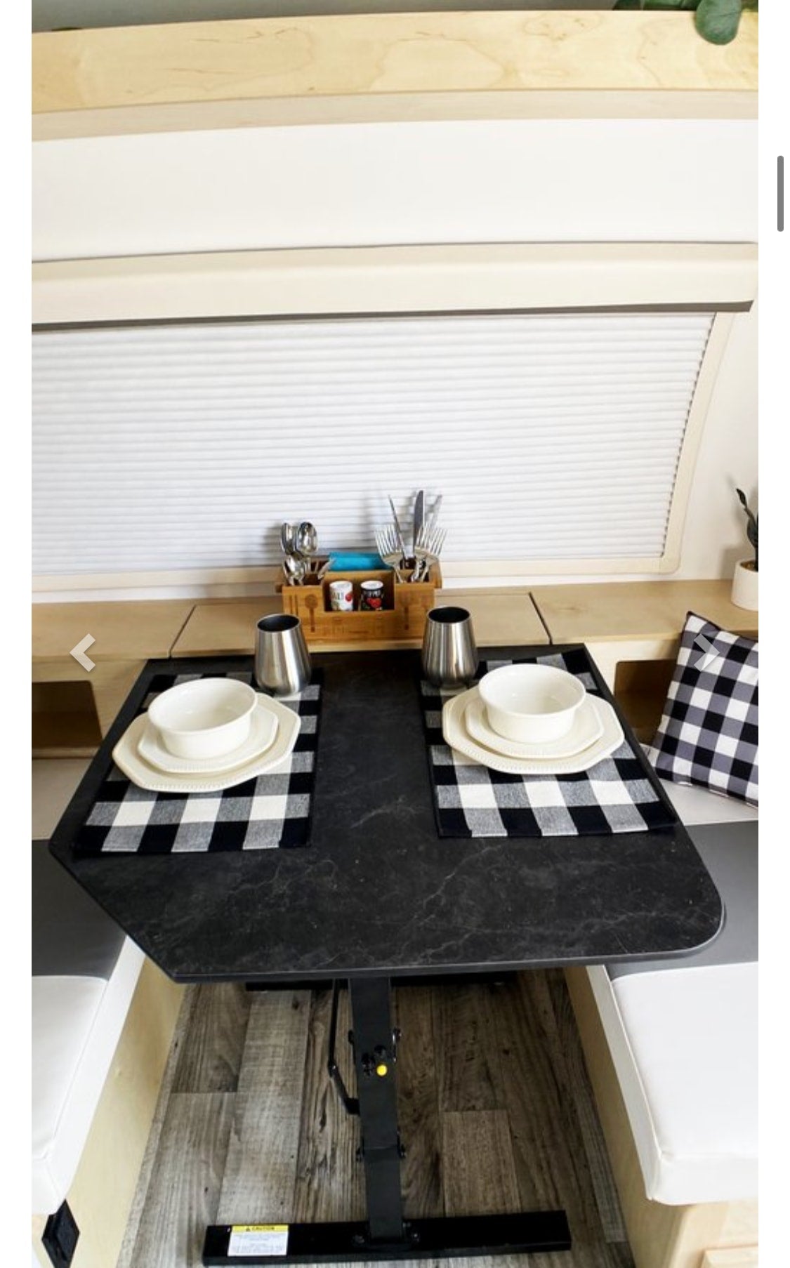 An RV rental's compact dining area features a black table set for two, with placemats and cutlery, flanked by benches.