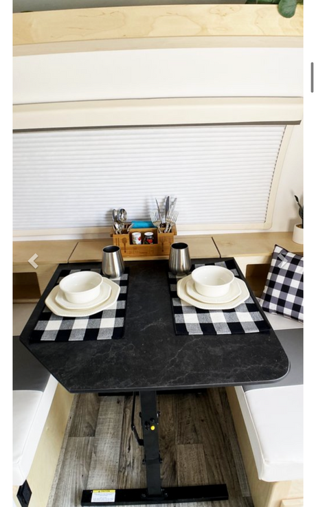 An RV rental's compact dining area features a black table set for two, with placemats and cutlery, flanked by benches.