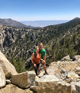 A couple smiles on a sunny mountain hike, overlooking a vast, treed valley. Ideal for an **rv rental** outdoor adventure.