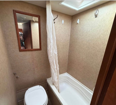 RV rental bathroom showing a compact toilet, shower, and tub combo with a mirror and hooks on textured walls.