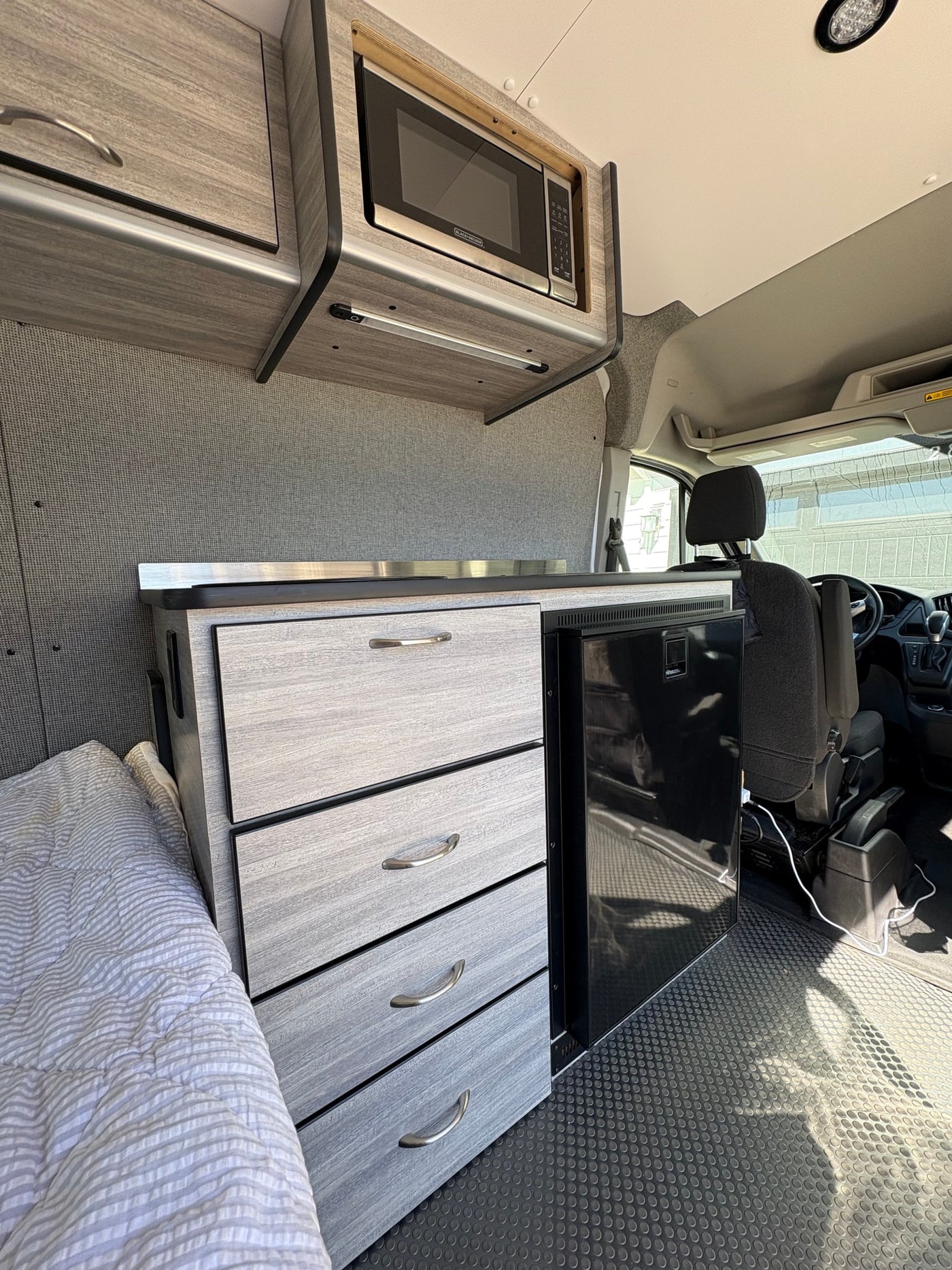Explore this RV rental's clever interior: compact kitchen with microwave, fridge, storage, and a comfy sleeping area. — photo 10