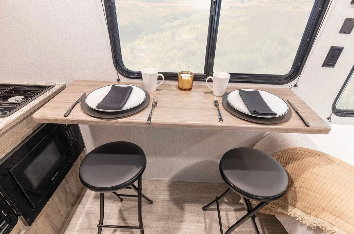 RV rental: Modern interior featuring a compact dining counter with two folding stools, full place settings, and kitchen amenities.