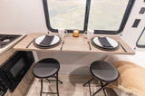 RV rental: Modern interior featuring a compact dining counter with two folding stools, full place settings, and kitchen amenities.