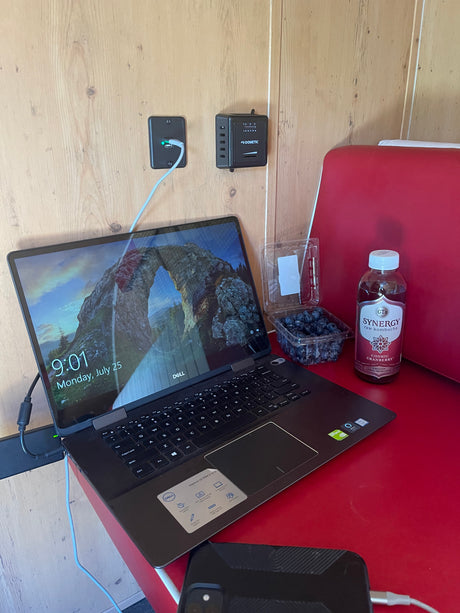 RV rental setup: Dell laptop, Dometic controls, kombucha, and blueberries on a red table, showing a mobile workspace.