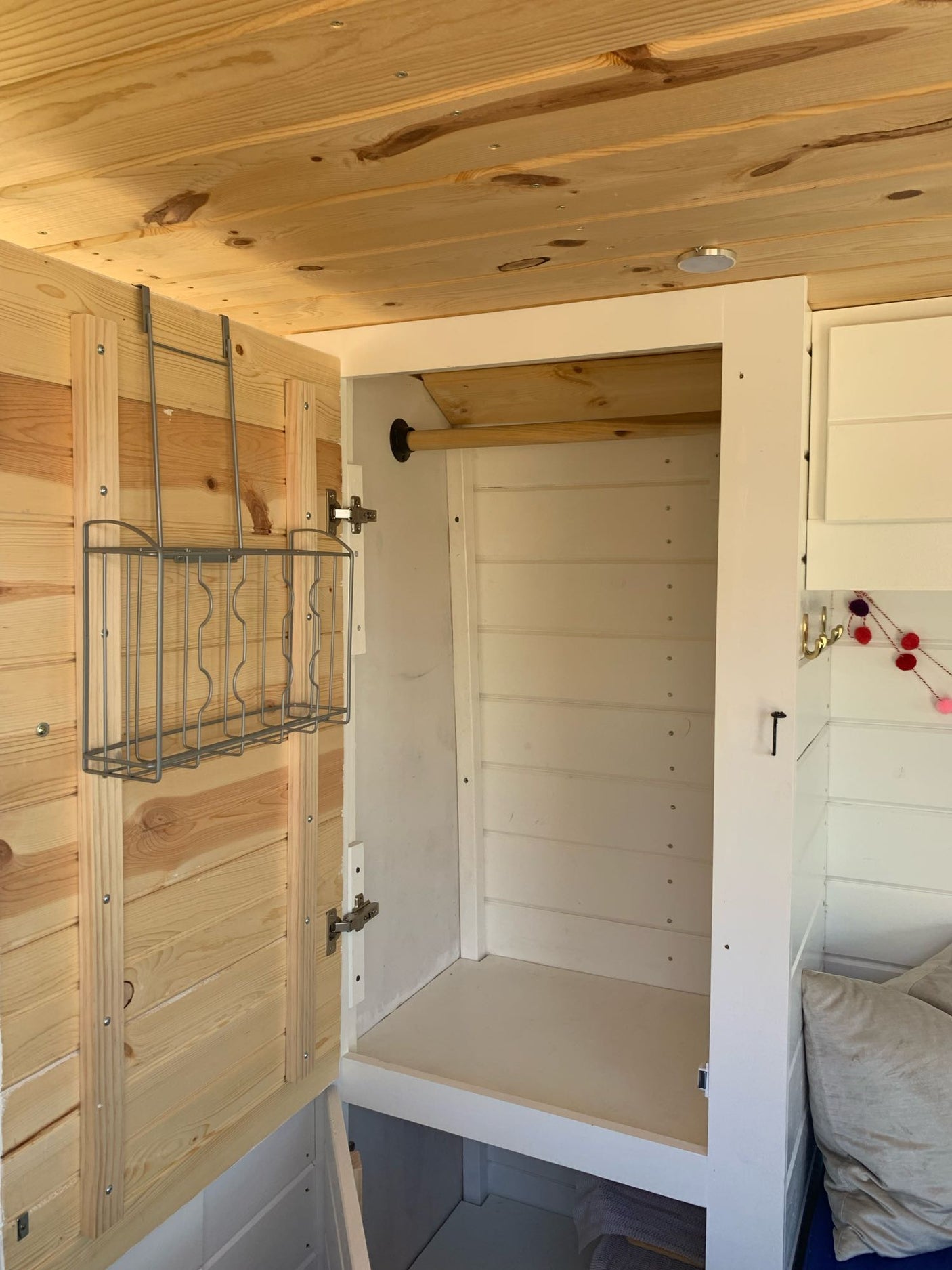 RV rental interior: an open white closet with natural wood walls/ceiling and a convenient door-mounted wire rack.