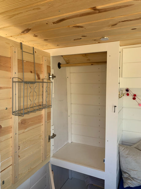 RV rental interior: an open white closet with natural wood walls/ceiling and a convenient door-mounted wire rack.